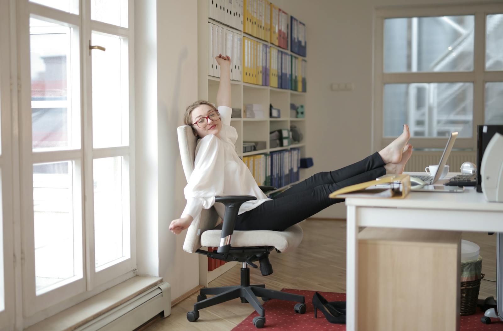 Cheerful woman relaxing in a modern office, barefoot with feet on the desk, enjoying a tranquil break.