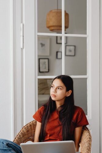 Woman thinking indoors in a chair with a laptop, epitomizing contemplation and calm.