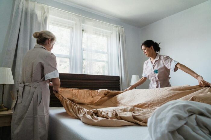 Two housekeepers professionally making a bed in a bright, comfortable room.